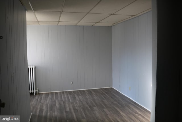 spare room with radiator, dark hardwood / wood-style floors, wooden walls, and a paneled ceiling