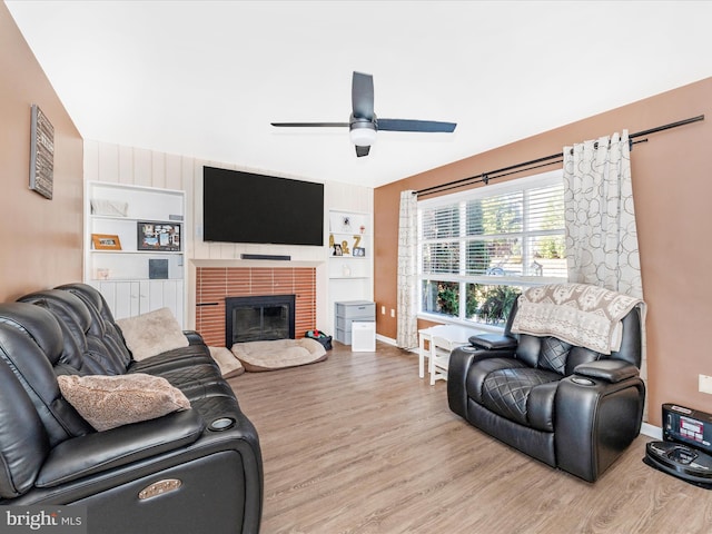 living room with built in features, light wood-type flooring, a brick fireplace, and ceiling fan