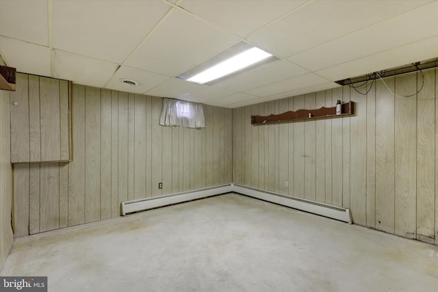 basement with a drop ceiling, baseboard heating, and wooden walls