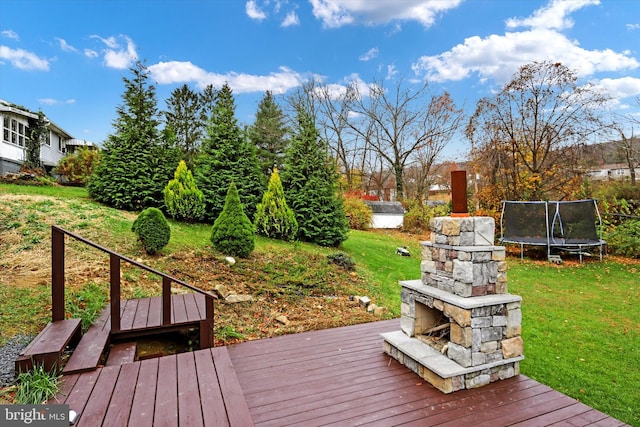 wooden terrace featuring an outdoor stone fireplace, a trampoline, and a yard