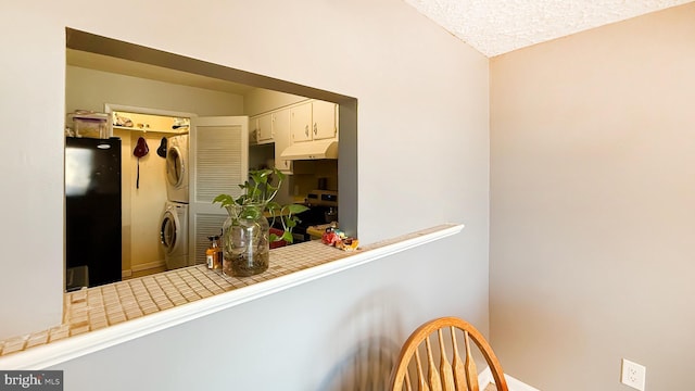 kitchen featuring black fridge, tile countertops, stacked washer / dryer, stainless steel range oven, and white cabinetry