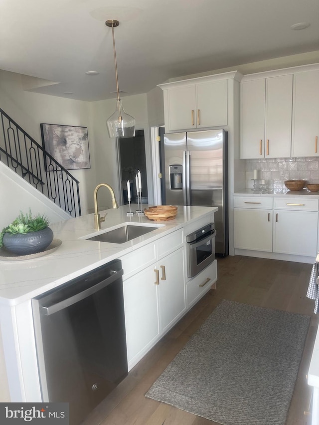 kitchen featuring a kitchen island with sink, sink, backsplash, appliances with stainless steel finishes, and white cabinets