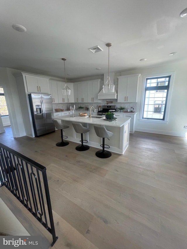 kitchen featuring hanging light fixtures, appliances with stainless steel finishes, white cabinetry, and custom range hood