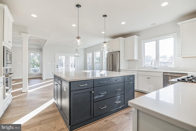 kitchen featuring white cabinetry, appliances with stainless steel finishes, ornate columns, hanging light fixtures, and a center island