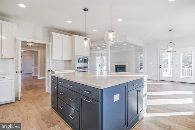 kitchen with stainless steel appliances, decorative light fixtures, decorative backsplash, white cabinets, and light hardwood / wood-style flooring