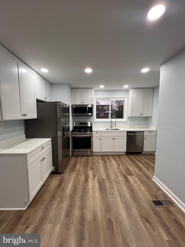 kitchen featuring white cabinetry, sink, hardwood / wood-style flooring, and appliances with stainless steel finishes