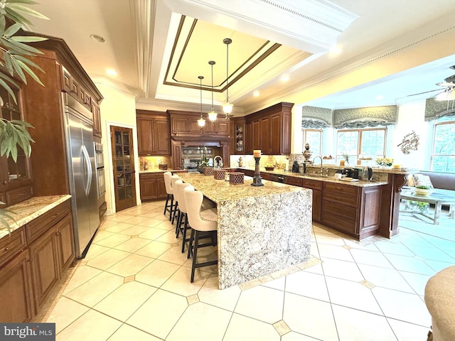 kitchen featuring stainless steel built in fridge, a center island with sink, crown molding, hanging light fixtures, and sink