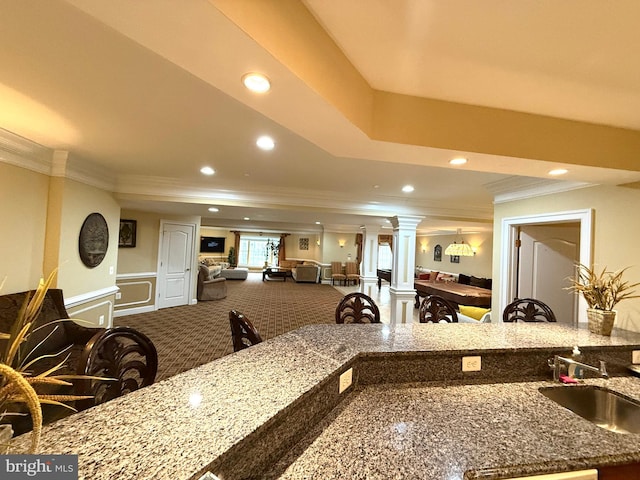 kitchen featuring ornamental molding, carpet flooring, stone counters, sink, and decorative columns