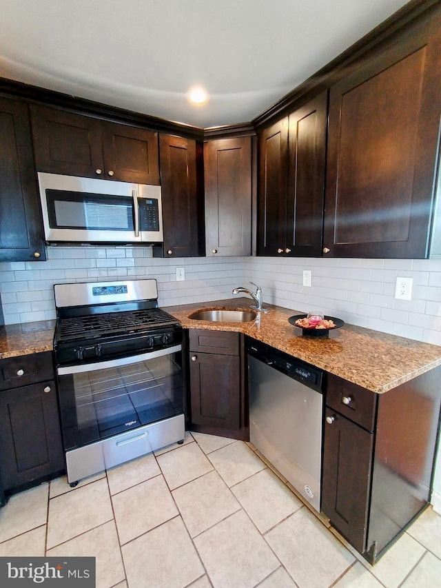 kitchen featuring stainless steel appliances, sink, light stone countertops, dark brown cabinets, and decorative backsplash