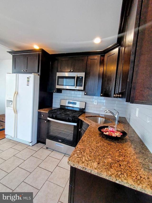 kitchen with stainless steel appliances, light tile patterned floors, tasteful backsplash, light stone countertops, and dark brown cabinets