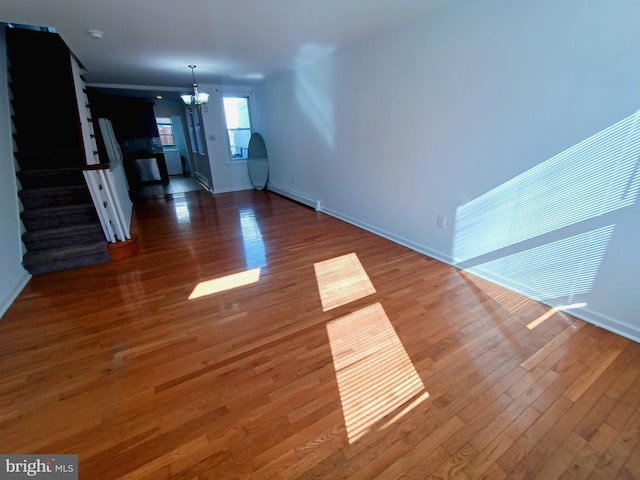 unfurnished living room with a baseboard heating unit, hardwood / wood-style flooring, and an inviting chandelier