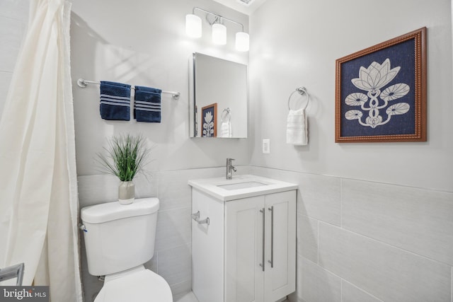 bathroom featuring toilet, vanity, and tile walls