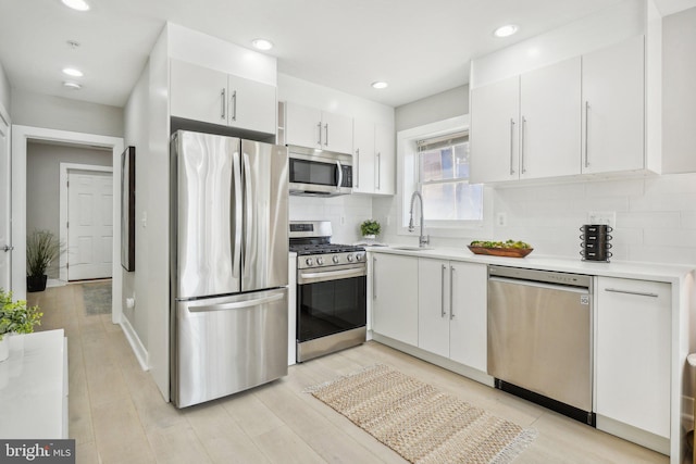 kitchen featuring stainless steel appliances, light hardwood / wood-style floors, sink, tasteful backsplash, and white cabinets