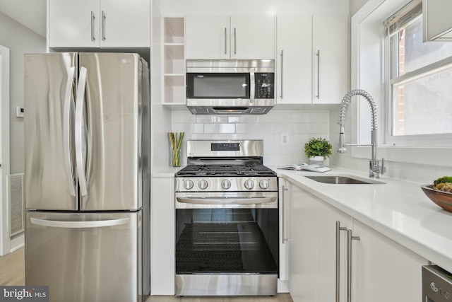 kitchen with stainless steel appliances, white cabinets, sink, backsplash, and light wood-type flooring