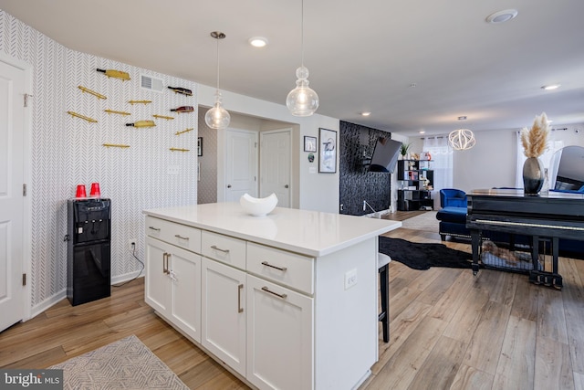 kitchen featuring white cabinets, decorative light fixtures, light hardwood / wood-style flooring, and a kitchen island