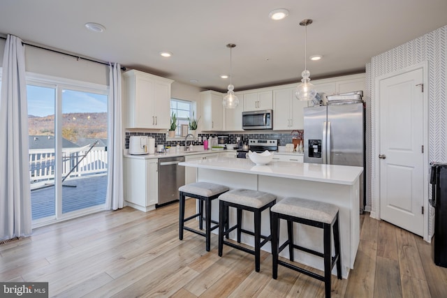 kitchen with white cabinets, decorative light fixtures, light wood-type flooring, and appliances with stainless steel finishes