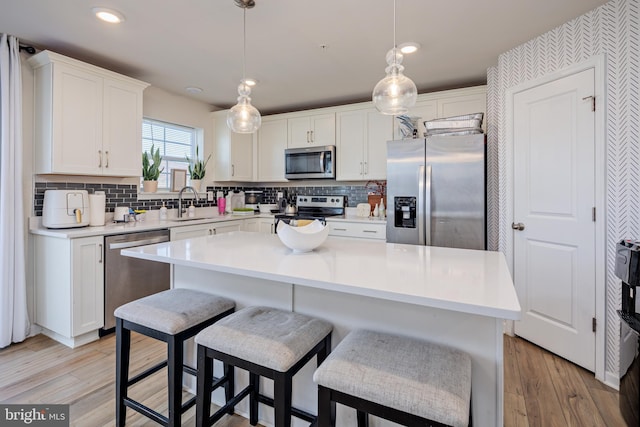 kitchen featuring white cabinets, sink, decorative light fixtures, a kitchen island, and stainless steel appliances