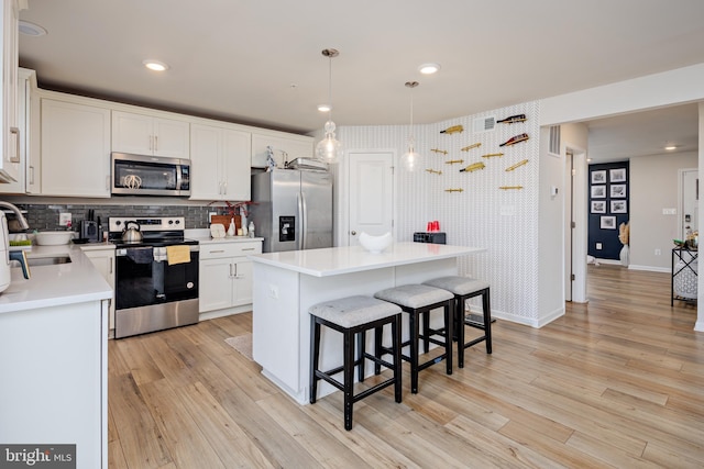 kitchen with light wood-type flooring, appliances with stainless steel finishes, a center island, and white cabinets