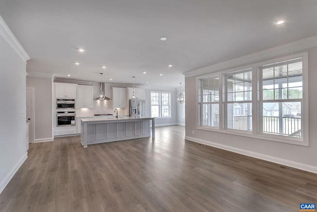 kitchen featuring crown molding, stainless steel appliances, pendant lighting, wall chimney exhaust hood, and a kitchen island with sink