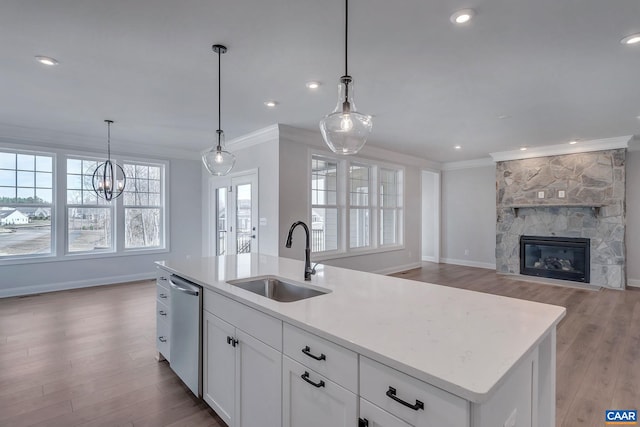 kitchen with light wood-type flooring, sink, a center island with sink, and a fireplace