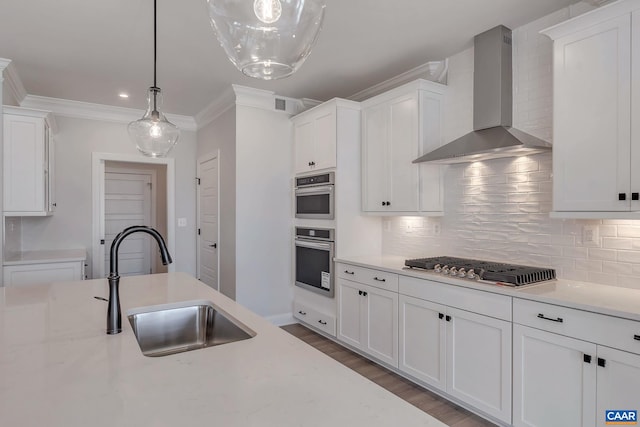 kitchen featuring white cabinetry, hanging light fixtures, sink, and wall chimney range hood