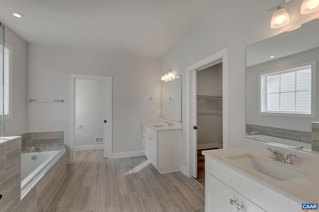 bathroom with vanity, tiled tub, and wood-type flooring