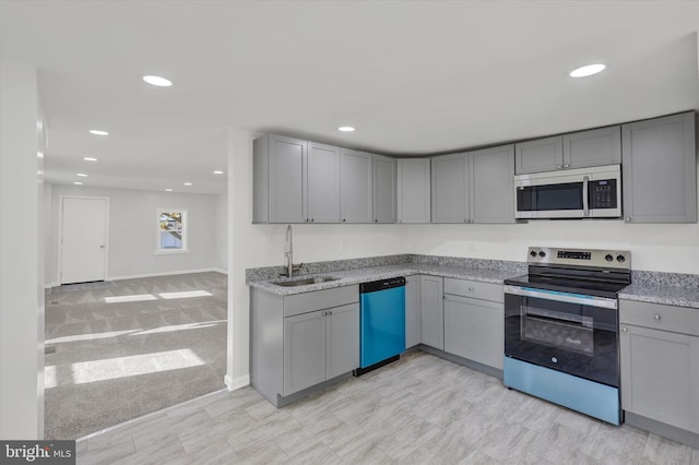 kitchen with sink, light stone counters, appliances with stainless steel finishes, gray cabinets, and light colored carpet