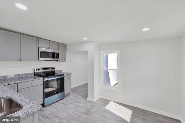 kitchen featuring gray cabinetry, light stone counters, and stainless steel appliances