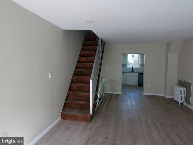 staircase featuring hardwood / wood-style floors, radiator heating unit, and sink