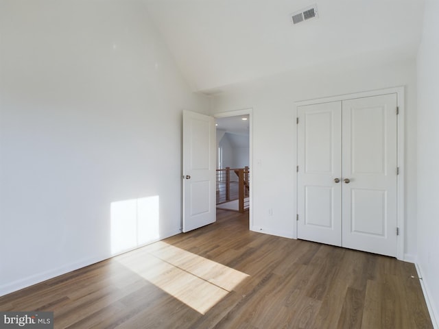 unfurnished bedroom featuring vaulted ceiling, hardwood / wood-style floors, and a closet