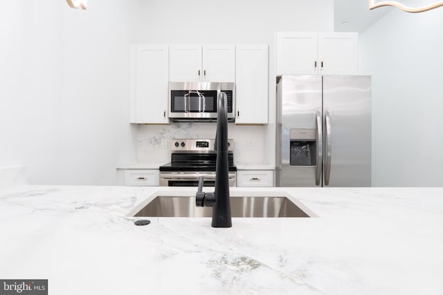 kitchen with white cabinetry, sink, light stone counters, appliances with stainless steel finishes, and backsplash