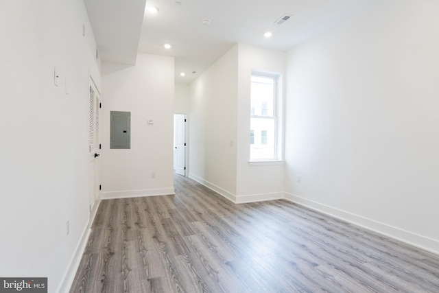 spare room with light wood-type flooring, electric panel, and a towering ceiling