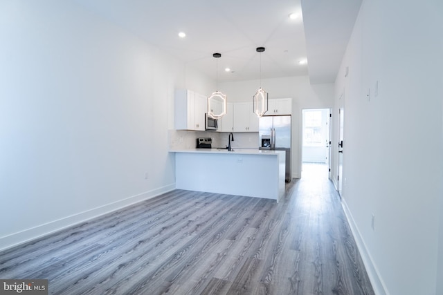 kitchen with light hardwood / wood-style floors, appliances with stainless steel finishes, kitchen peninsula, white cabinets, and pendant lighting