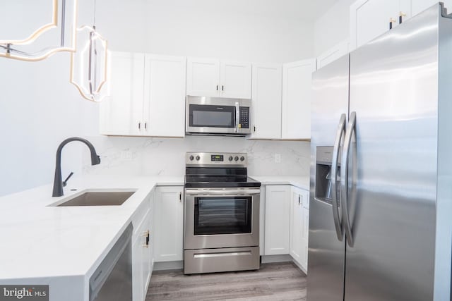 kitchen with stainless steel appliances, white cabinets, sink, and decorative light fixtures