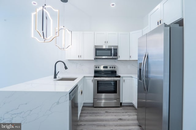 kitchen with stainless steel appliances, white cabinets, sink, light stone countertops, and decorative light fixtures