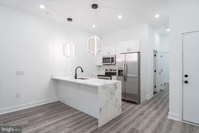 kitchen with stainless steel appliances, sink, kitchen peninsula, white cabinets, and pendant lighting