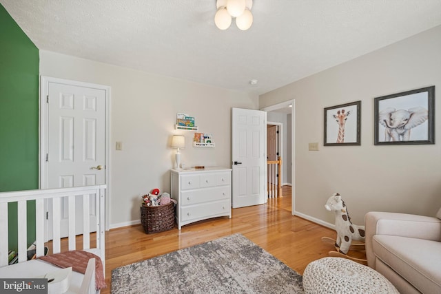 bedroom with a textured ceiling, hardwood / wood-style floors, and a crib