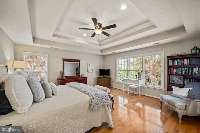 bedroom with ornamental molding, a textured ceiling, a raised ceiling, hardwood / wood-style floors, and ceiling fan