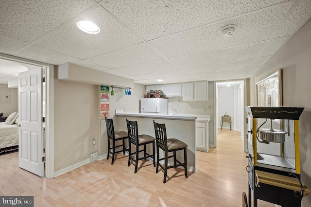 kitchen with white cabinetry, kitchen peninsula, a kitchen breakfast bar, white fridge, and light wood-type flooring