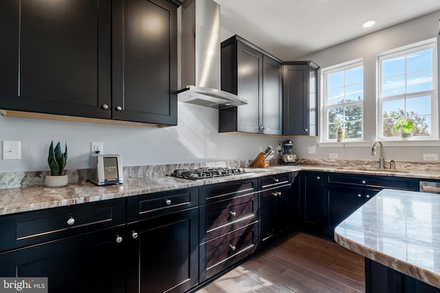 kitchen featuring dark wood-type flooring, stainless steel gas stovetop, light stone counters, sink, and wall chimney range hood