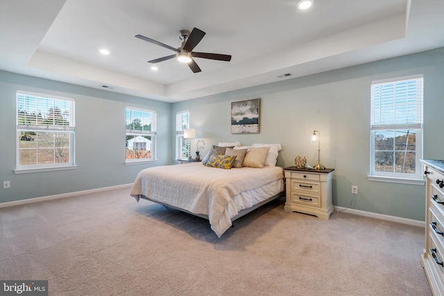 bedroom featuring light colored carpet, multiple windows, a raised ceiling, and ceiling fan