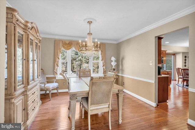 dining room with ornamental molding, light wood-type flooring, and a notable chandelier