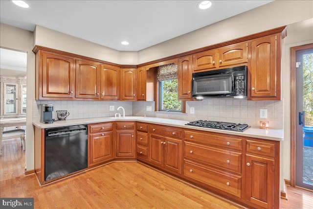 kitchen featuring light wood-type flooring, sink, black appliances, and decorative backsplash