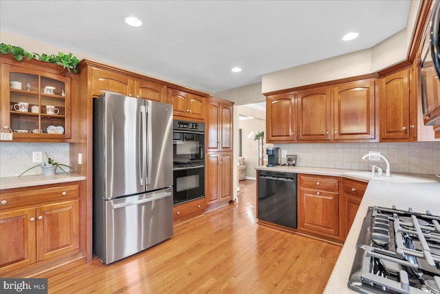 kitchen with black appliances, backsplash, sink, and light hardwood / wood-style floors