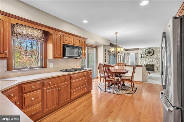 kitchen featuring a stone fireplace, a notable chandelier, light wood-type flooring, appliances with stainless steel finishes, and decorative light fixtures