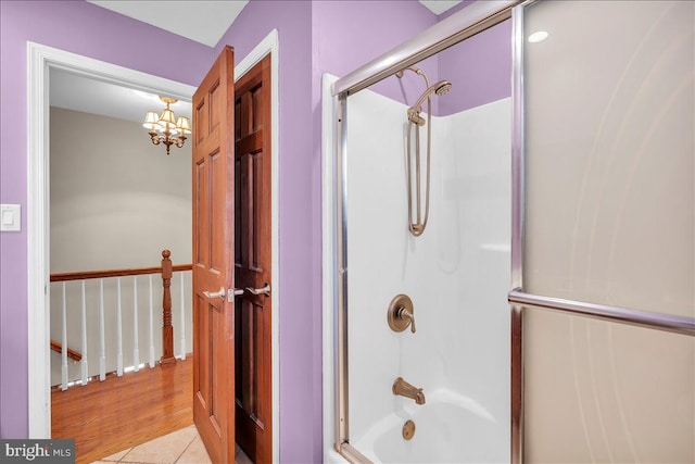 bathroom with hardwood / wood-style flooring, an inviting chandelier, and enclosed tub / shower combo