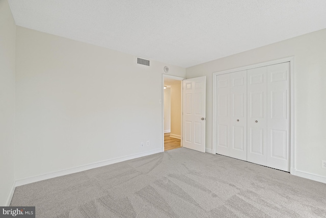 unfurnished bedroom with light colored carpet, a textured ceiling, and a closet