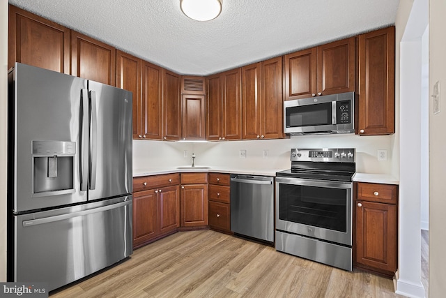 kitchen with appliances with stainless steel finishes, a textured ceiling, light hardwood / wood-style floors, and sink