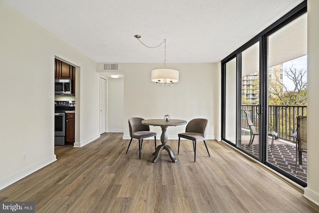 dining area with a textured ceiling, wood-type flooring, a notable chandelier, and a wall of windows