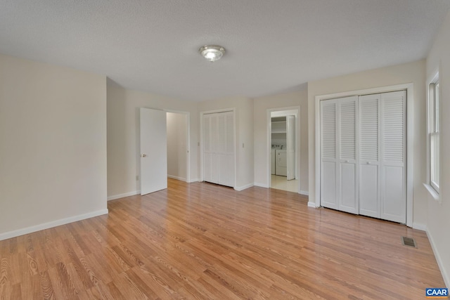 unfurnished bedroom with light hardwood / wood-style floors, two closets, a textured ceiling, and washer and clothes dryer